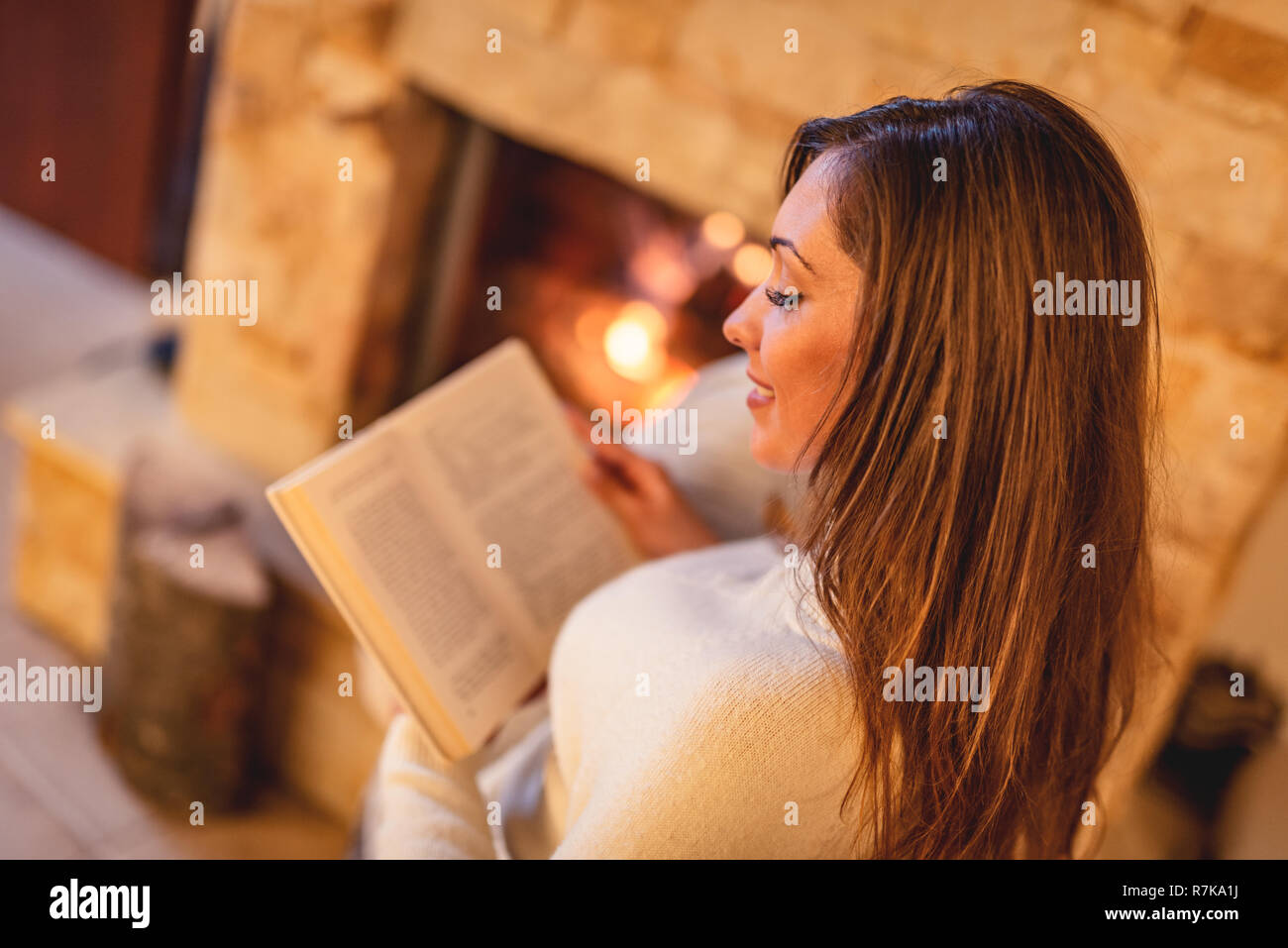 Schöne junge lächelnde Frau mit Buch und genießen am Kamin. Stockfoto