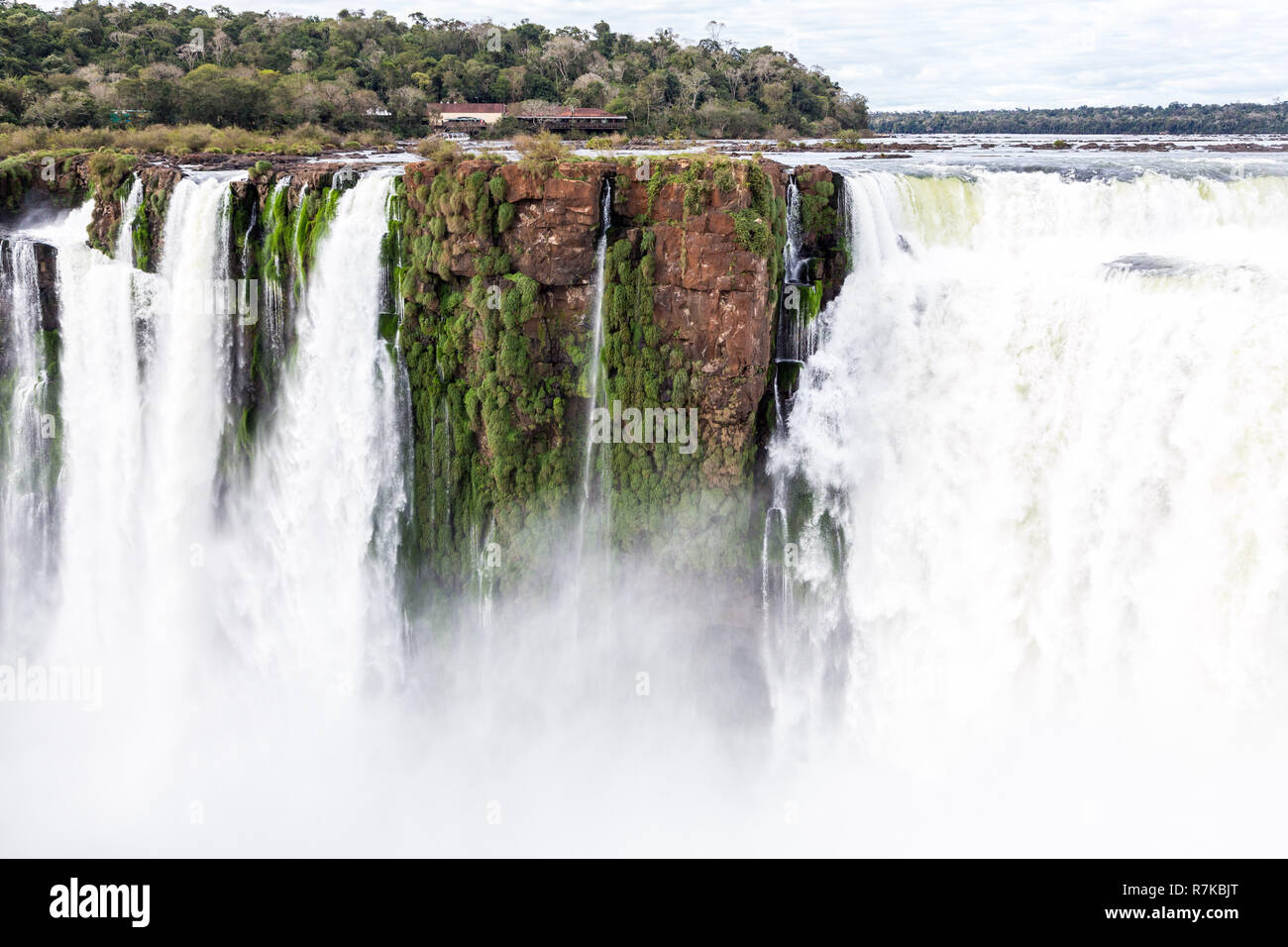 Aufbauend auf einem Felsen über einem ​Waterfall. Winter Blick auf die Iguazu Fälle Teufelsschlund unter schweren Wolken führen. Die Grenze zwischen Brasilien und Argentinien. Stockfoto