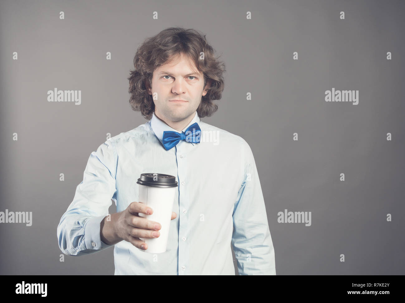 Close up Portrait von glücklich aussehenden Mann im blauen Hemd mit Papier Tasse Kaffee am Morgen. Guten Morgen mit Kaffee. Takeaway Kaffee, Zeit für die Kaffeepause. Kellner bietet Coffee-to-go. Getönt. Kopieren Sie Platz. Stockfoto