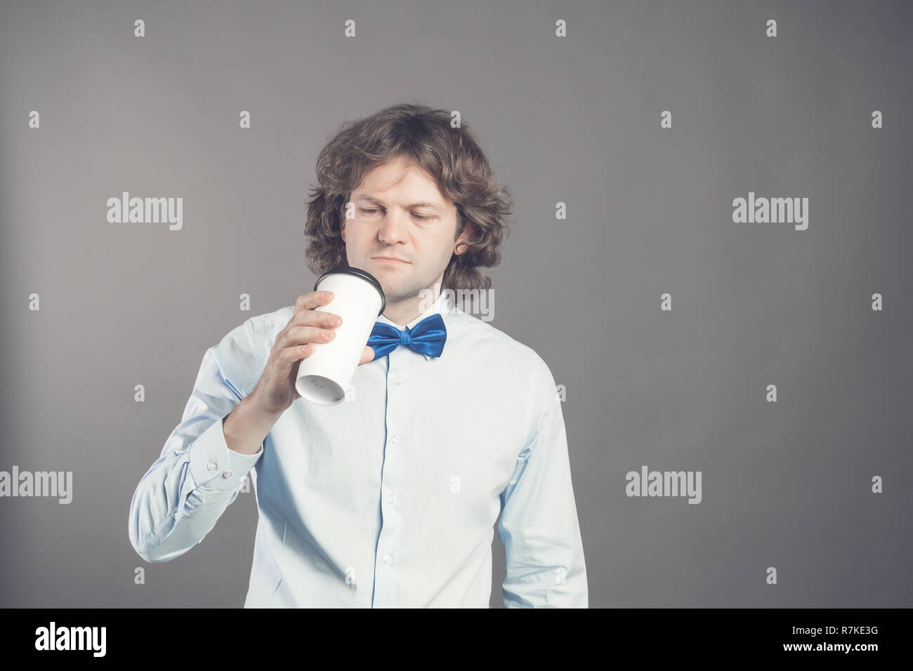 Close up Portrait von glücklich aussehenden Mann im blauen Hemd mit Papier Tasse Kaffee am Morgen. Guten Morgen mit Kaffee. Takeaway Kaffee, Zeit für die Kaffeepause. Kerl wird Kaffee aus Einweg Kelch zu trinken, Stockfoto