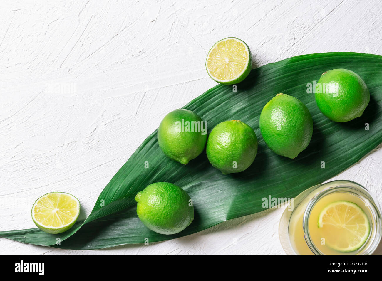 Bündel von Limes auf einer großen, grünen Blatt und ein Glas mit frisch gepressten Limettensaft, auf einem weißen Hintergrund. Oben Ansicht mit kopieren. Detox Kontext. Stockfoto