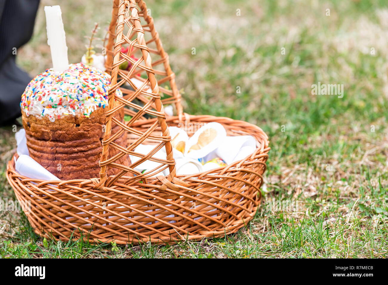 Eier und Kulich Russisch-orthodoxe Ostern Segen wicker Strohkorb, Kerze auf Gras Boden außen an der Kirche, Beine Stockfoto