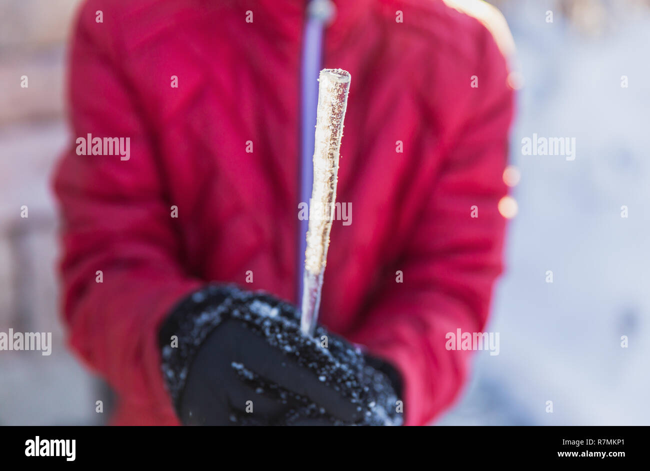 Kind mit schwarzen Handschuhe und eine rote Jacke hält eine icecicle im Winter. Stockfoto