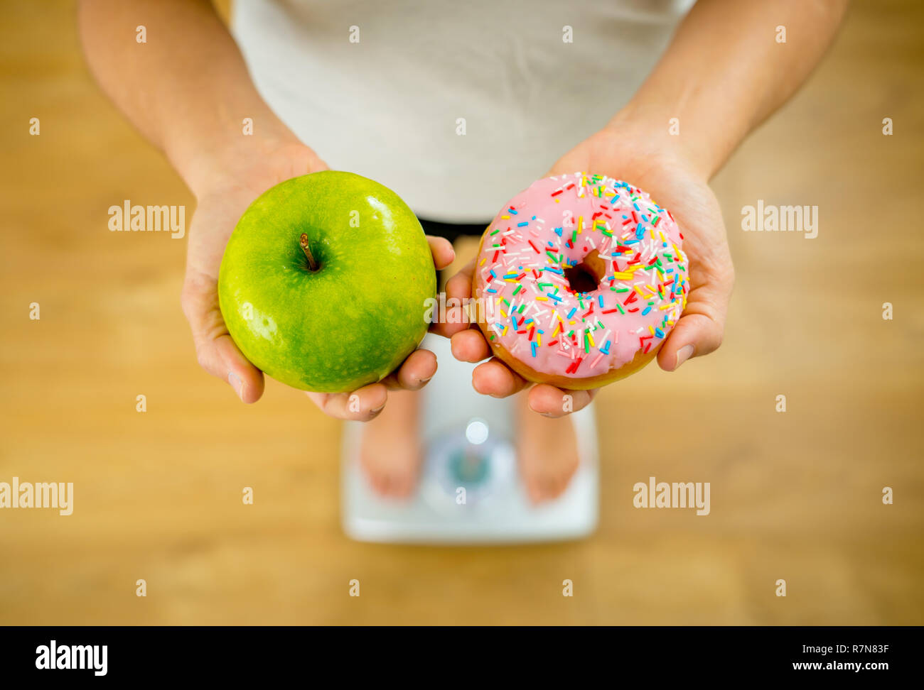 Nahaufnahme von Frau auf der Skala, in die Hände von Apple und Krapfen, die Wahl zwischen gesunden ungesunden essen Dessert während der Messung Körpergewicht in der Mutter Stockfoto
