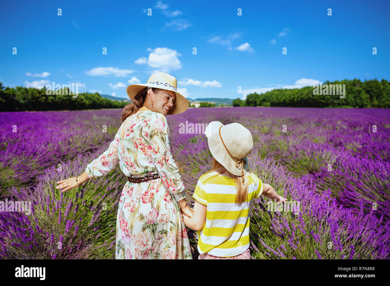 Lächelnd stilvolle Mutter und Kind berühren Lavendel gegen Lavendelfeld in der Provence, Frankreich. lavendel Feld ist die berühmteste Sehenswürdigkeit in der Provence. Stockfoto