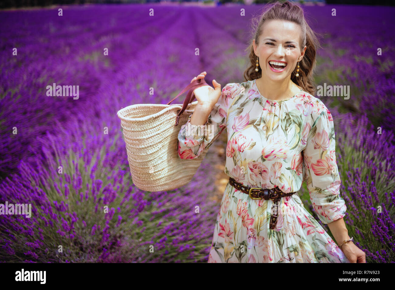 Portrait von Happy stilvolle Frau mit Stroh Beutel in lavendelfeld in der Provence, Frankreich. Frau genießen, eine Zeit der Blüte Lavendel Stockfoto