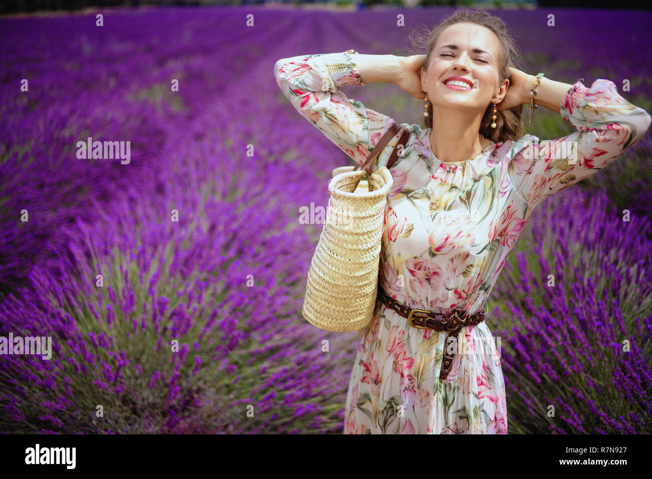 Portrait von entspannten modernen Frau im langen Kleid mit Stroh Beutel gegen Lavendelfeld in der Provence, Frankreich. Frau genießen den Duft von Lavendel Blumen Stockfoto