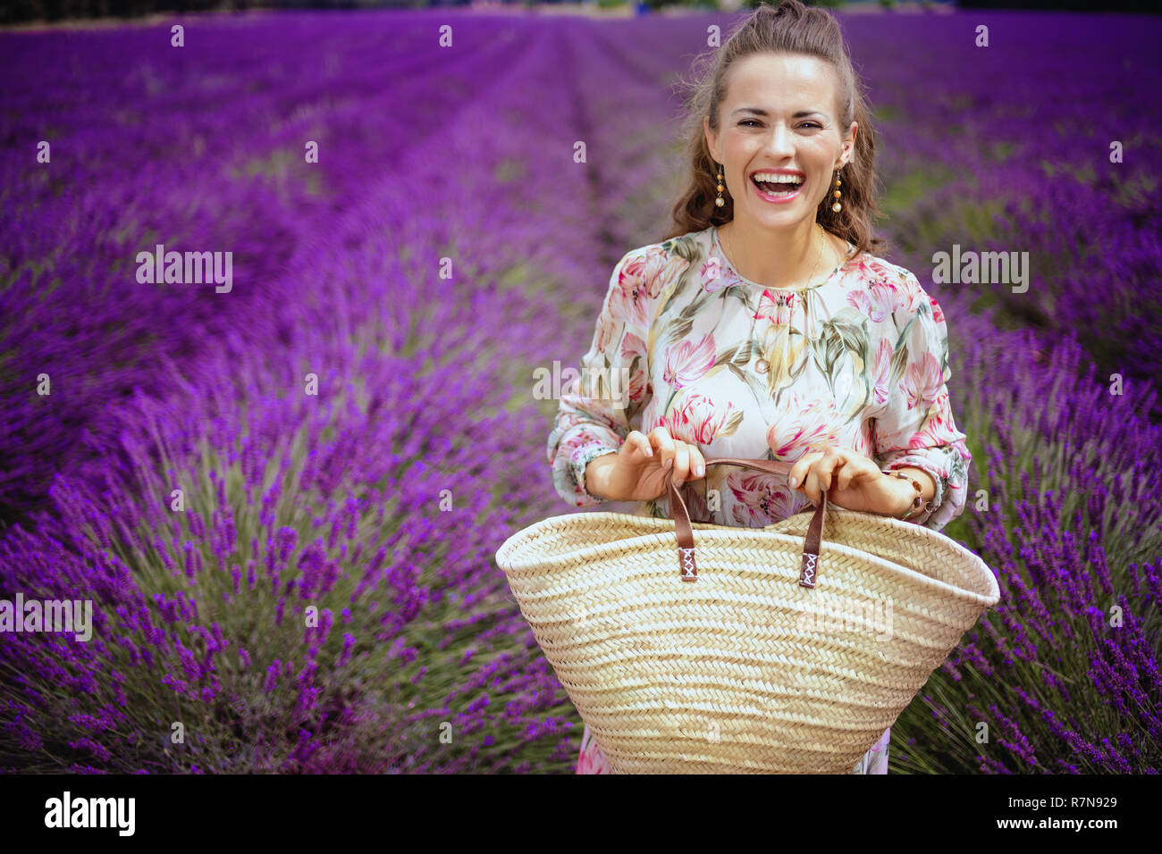 Porträt der Frau in geblümten Kleid mit Stroh Beutel gegen Lavendelfeld in der Provence, Frankreich. Düfte von Lavendel Blumen, Plateau von Valensole landet Stockfoto