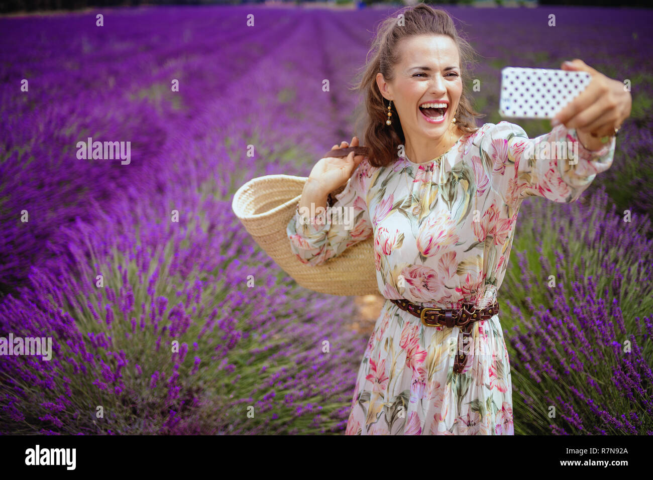 Glückliche junge Frau mit Stroh Beutel unter selfie mit Handy in lavendelfeld in der Provence, Frankreich. Reisen Fotos vor dem Hintergrund einer bloomin Stockfoto