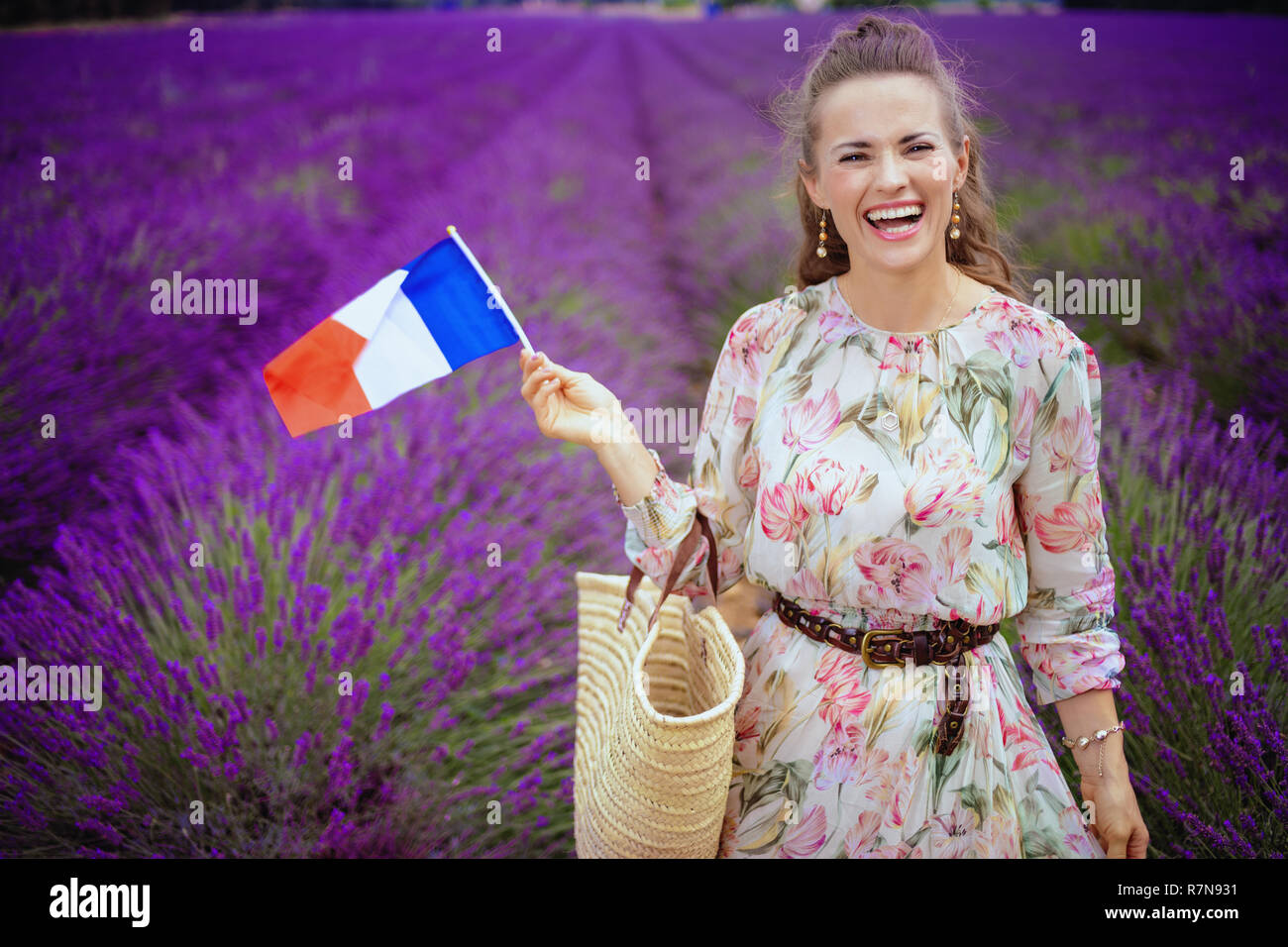 Glückliche Frau im langen Kleid mit Stroh Beutel, die französische Flagge gegen Lavendelfeld in der Provence, Frankreich. Der Sommer ist die Zeit Traum in die Realität umzusetzen - e Stockfoto