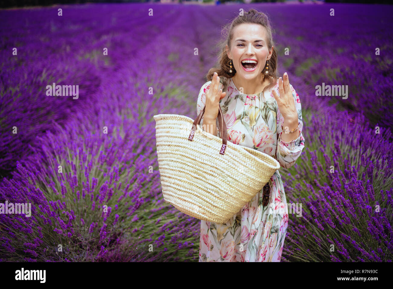 Aufgeregt, elegante Frau mit Stroh Beutel in lavendelfeld in der Provence, Frankreich. Eine unerwartete Überraschung - eine ungeplante Reise zu den duftenden Lavendel Valens Stockfoto