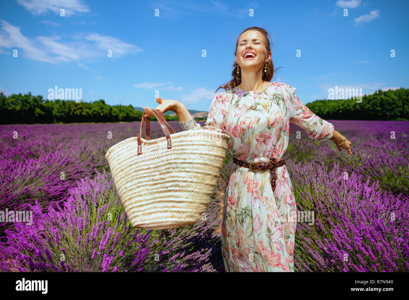 Gerne trendy Frau in langen Kleid mit Stroh Beutel voller Freude gegen Lavendelfeld in der Provence, Frankreich. Aufgeregt Frau gerne schöne zu besuchen Stockfoto