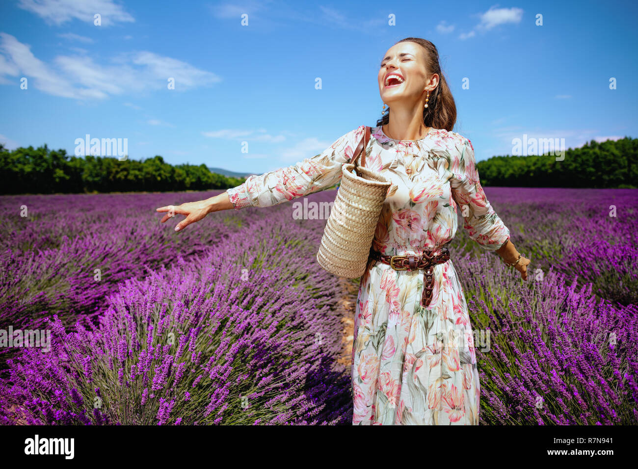 Aufgeregt, moderne Frau im Sommerkleid mit Stroh Beutel voller Freude gegen Lavendelfeld in der Provence, Frankreich. Tag Sommer im typisch provenzalischen Landschaften. Stockfoto