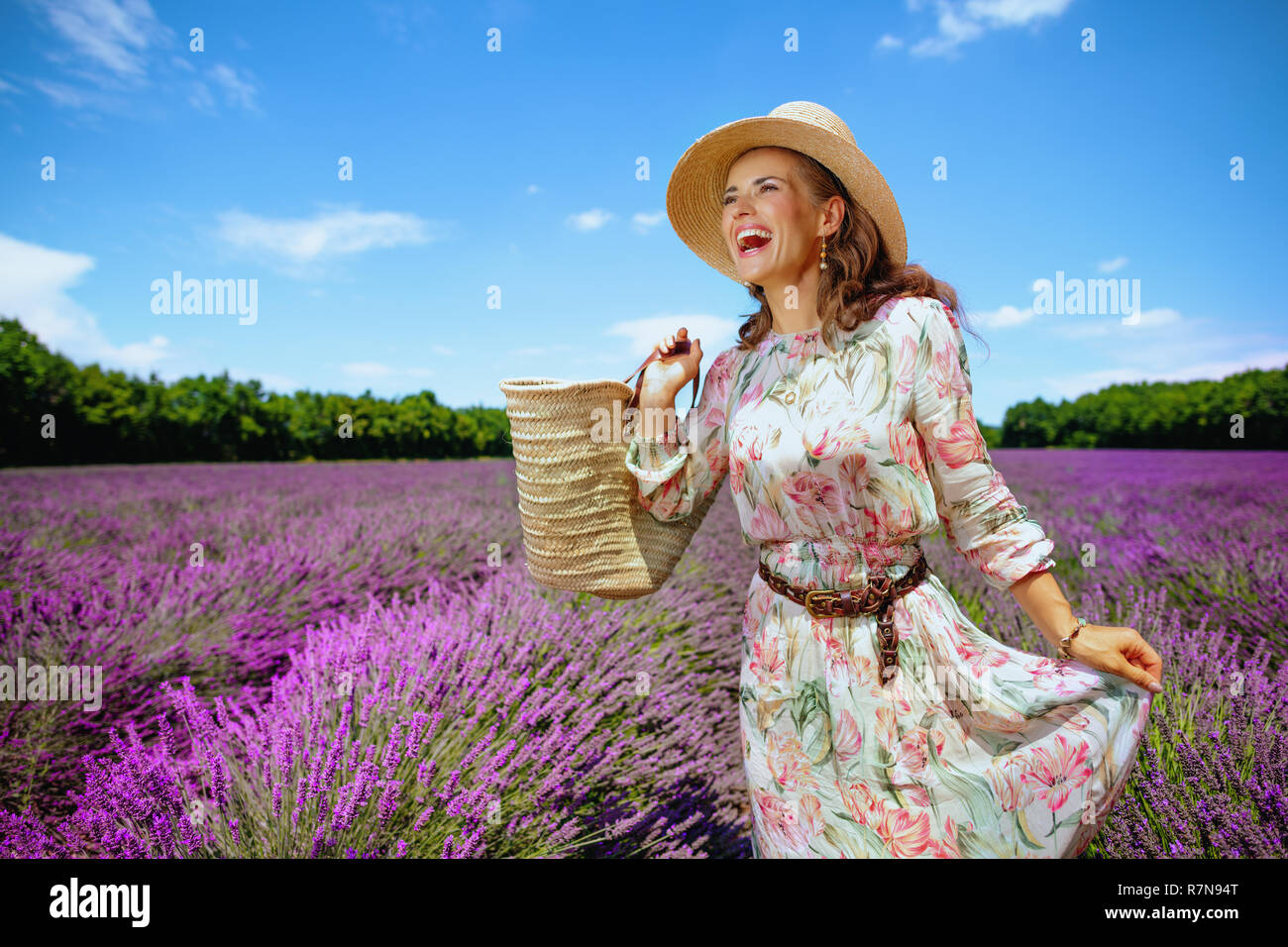 Aufgeregt, elegante Frau mit Stroh Beutel Blick in die Ferne in lavendelfeld in der Provence, Frankreich. Frau mit Picknick Tasche weg weg von der Stockfoto