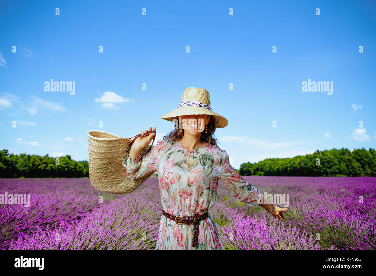Trendy Frau in geblümten Kleid mit Stroh Beutel voller Freude an lavendelfeld in der Provence, Frankreich. Frau touristische finden perfekte Lavendelfeld von Ro Reisen Stockfoto