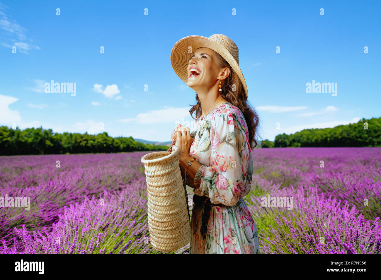 Happy Elegant Frau in langen Kleid mit Stroh Beutel schauen in die Ferne gegen Lavendelfeld in der Provence, Frankreich. Super reisen Fotos von Fran Stockfoto