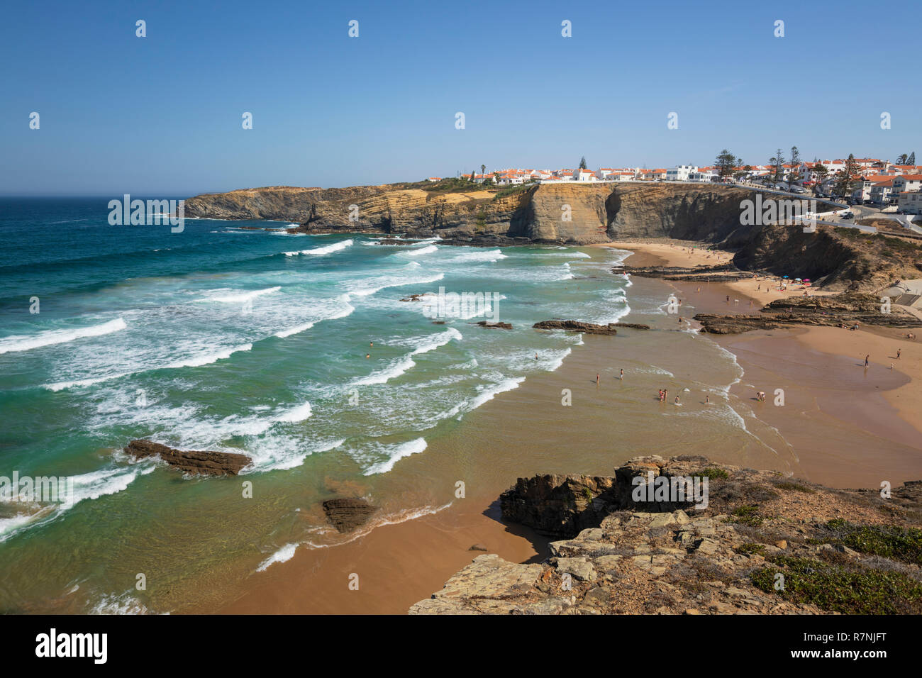 Weiß getünchte Stadt auf Klippen über Strand und brechenden Wellen des Atlantik in der Mittagssonne, Zambujeira do Mar, Alentejo, Portugal, Europa Stockfoto