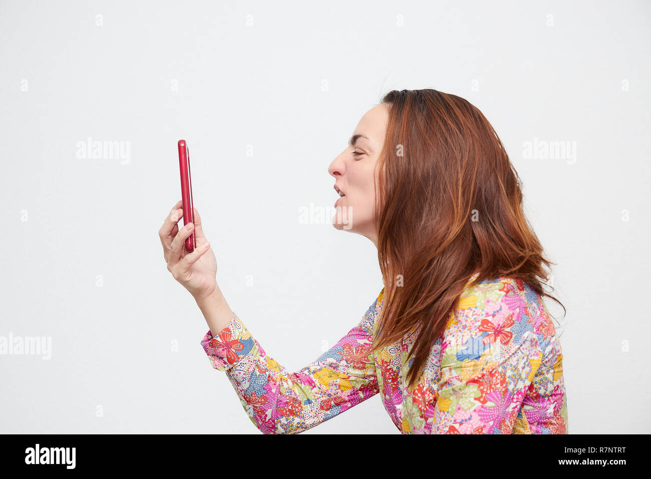 Porträt einer jungen Frau in Farbe Shirt auf einem Mobiltelefon auf einem weißen Hintergrund zu schreien. Stockfoto