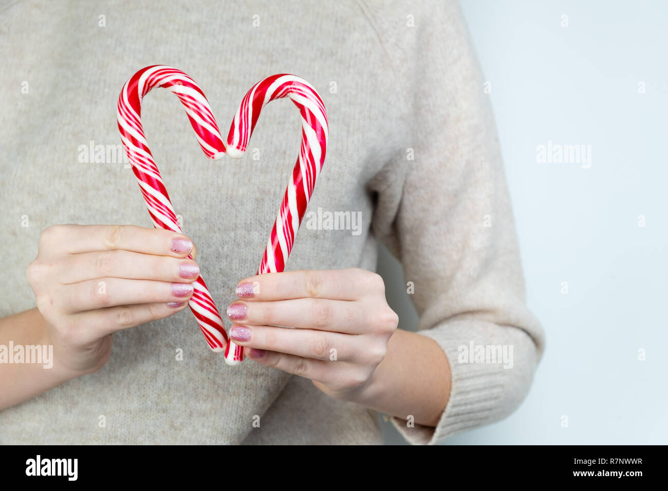 Liebe Konzept: Person hält zwei zuckerstangen, die Form des Herzens. Herz aus zwei weißen und roten Weihnachten Süßigkeiten. Stockfoto