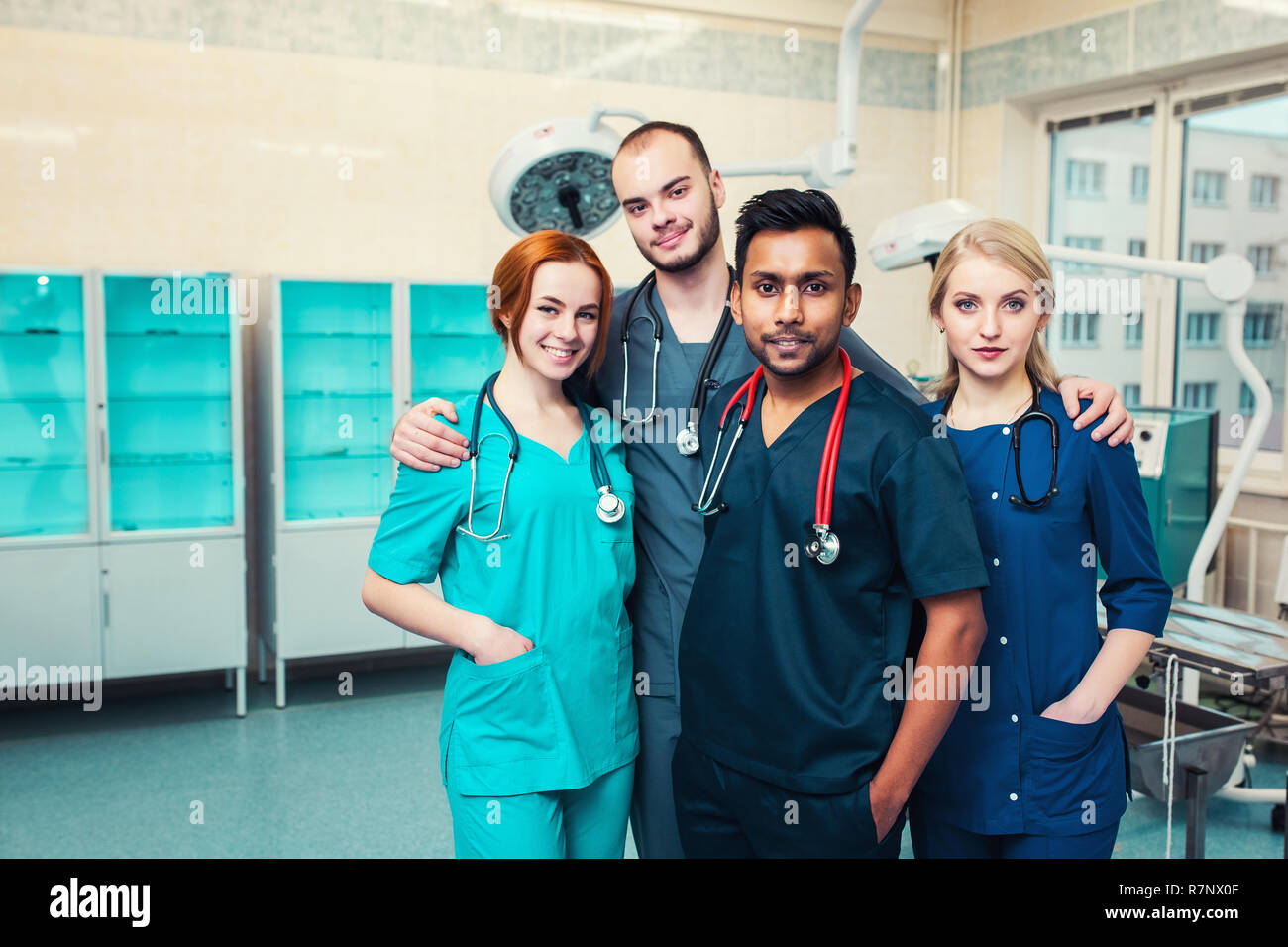 Gruppe junge Multirassischen Medizinstudenten mit Chirurgen umarmen, mit einem Lächeln in die Kamera. Krankenhaus OP-Saal in der backgroun Stockfoto