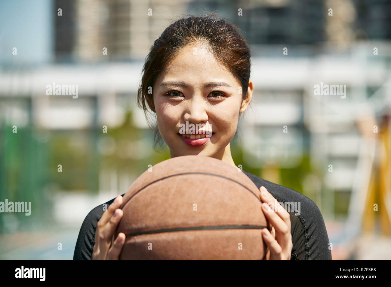 Outdoor Portrait von schönen jungen asiatischen Mädchen, dass eine Basketball an der Kamera schaut lächelnd. Stockfoto