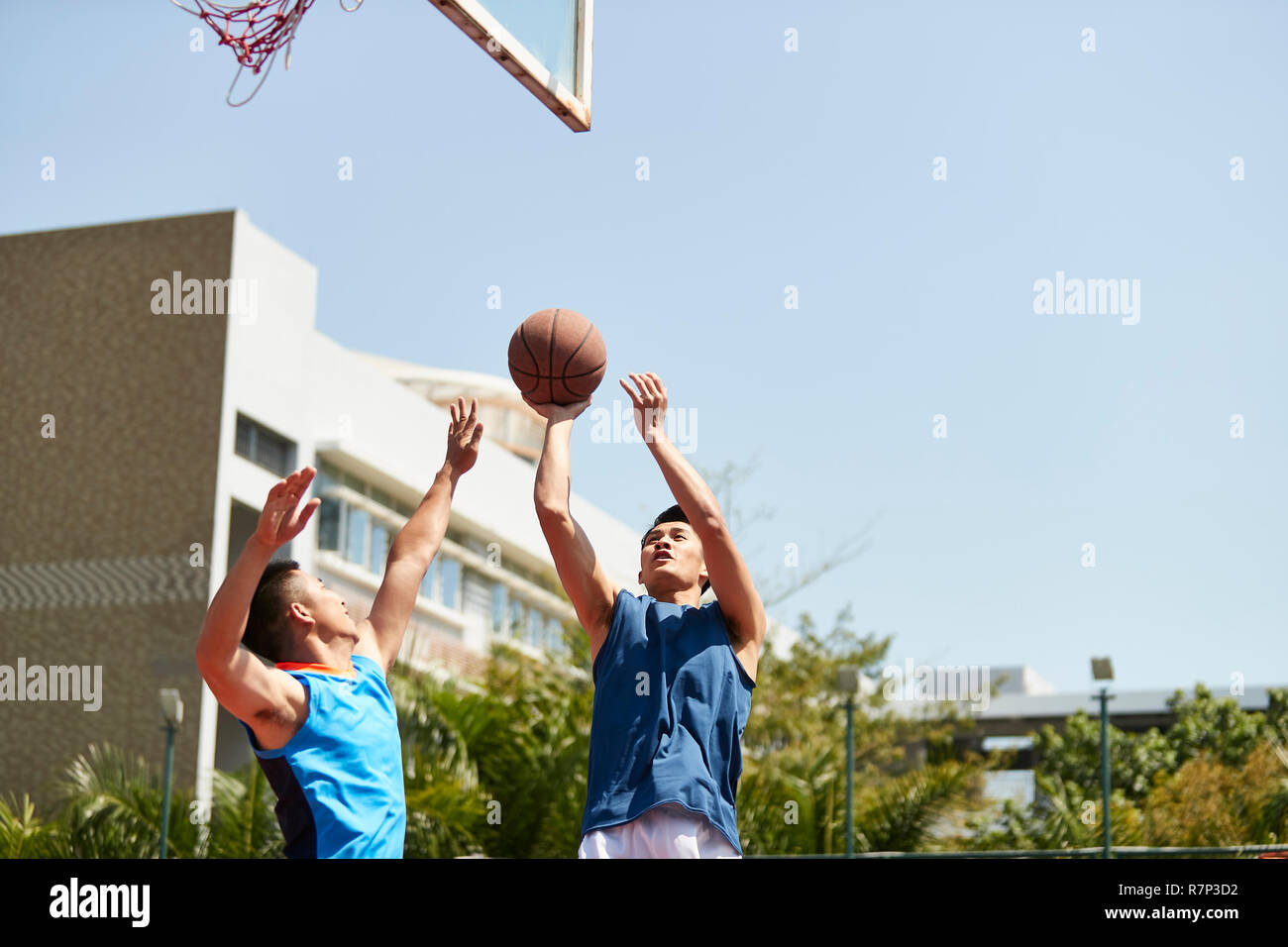 Jungen asiatischen Basketball Spieler schießt die Kugel über Defender auf im Hof. Stockfoto