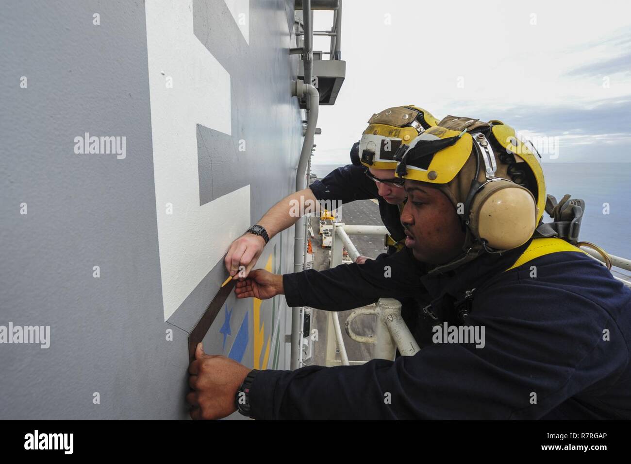 Indischer Ozean (30. März 2017) Quartiermeister 3. Klasse Robert Ahrns, rechts von Clare, Michigan, und Quartiermeister 2. Klasse Brandon Mingo, aus Darlington, S.C., zeichnen Sie die Umrisse für eine weiße Schlacht 'E' auf der Seite der Insel Überbau der amphibischen Angriff Schiff USS Makin Island (LHD 8). Die Schlacht "E" wird jedes Jahr während der Marine Schiffe verliehen deren Besatzungen konsequent Exzellenz in Kriegszeiten Fähigkeiten und optimale Mission Bereitschaft innerhalb ihrer Plattform und Region zeigen. Makin Island, das Flaggschiff für die Makin Island amphibische bereit Gruppe, mit der eingeschifften 11. Marine Expe Stockfoto