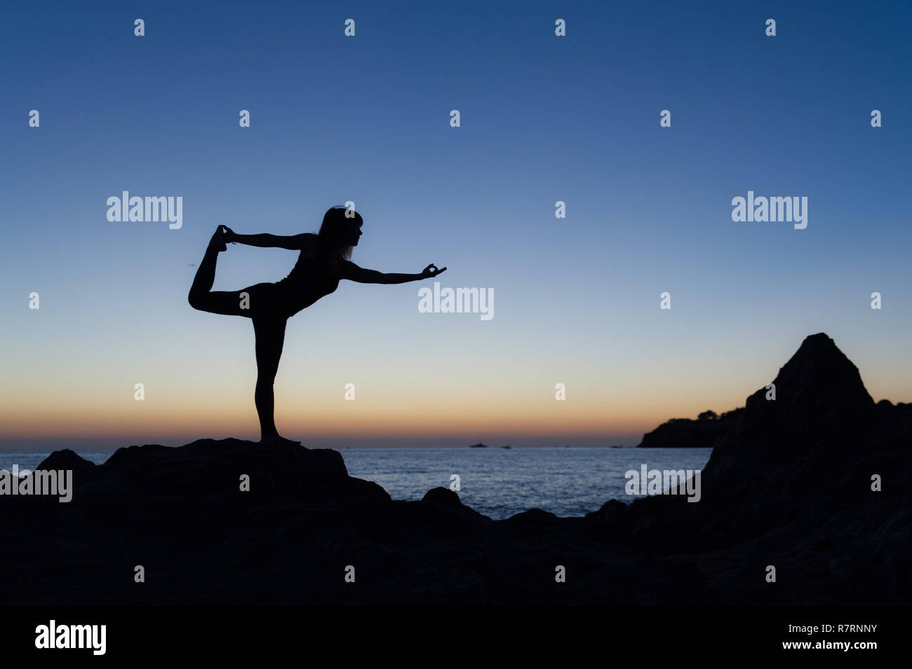 Argelès-sur-Mer (Frankreich). Jemand Yoga auf den Felsen vor der Racou Strand bei Sonnenaufgang. Schöne junge Frau mit langen b Stockfoto