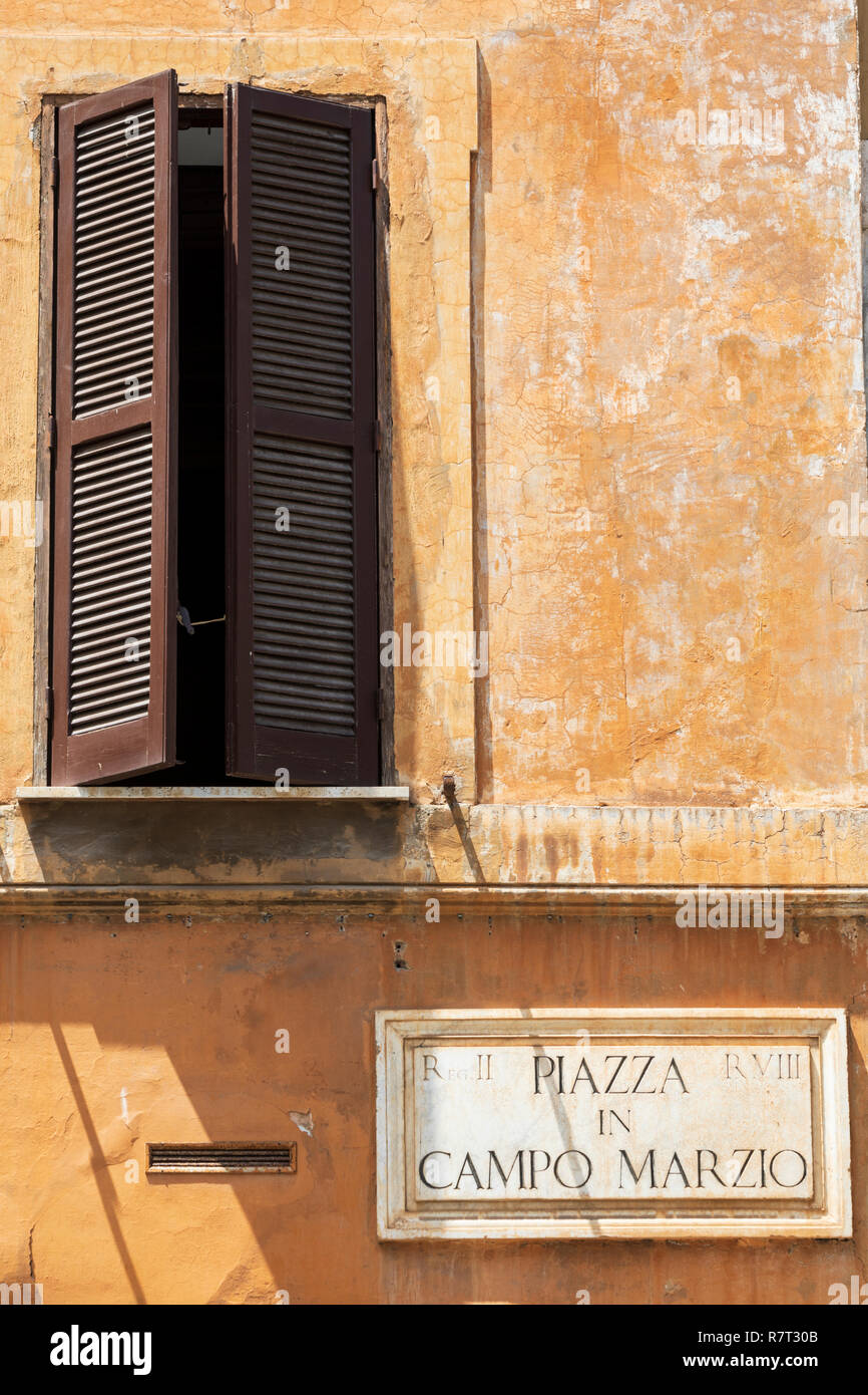 Ein offenes Fenster mit Fensterläden aus Holz in einer verwitterten Mauer an der Piazza Campo Marzio in Rom, Italien. Stockfoto