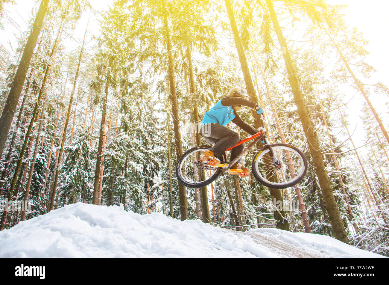 Silhouette eines Radfahrers in einem Sprung. Mountainbiken auf Wanderwegen in einem verschneiten Wald. Extreme Winter Sport. Bike Reiter fliegt durch die Luft, Stockfoto