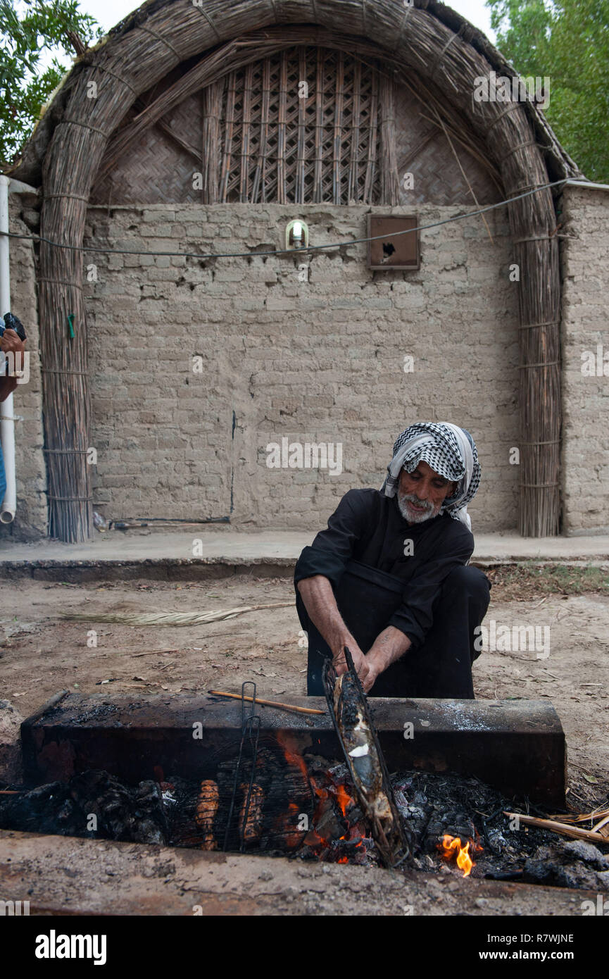 November 3, 2018 - Al-Chibayish, Sümpfe des südlichen Irak, Irak - Abu Haidar gesehen grillen Masgouf außerhalb einer Adobe Haus in Al-Chibayish im Südlichen Sümpfe des Irak. niedrige Wasserstände und erhöhten Salzgehalt reduziert und der Bestand wesentlich in der südlichen Sümpfe des Irak. Klimawandel, Deichbau in der Türkei und internen Misswirtschaft sind die Ursachen für eine schwere Dürre im südlichen Feuchtgebiete des Irak. Quelle: John wreford/SOPA Images/ZUMA Draht/Alamy leben Nachrichten Stockfoto