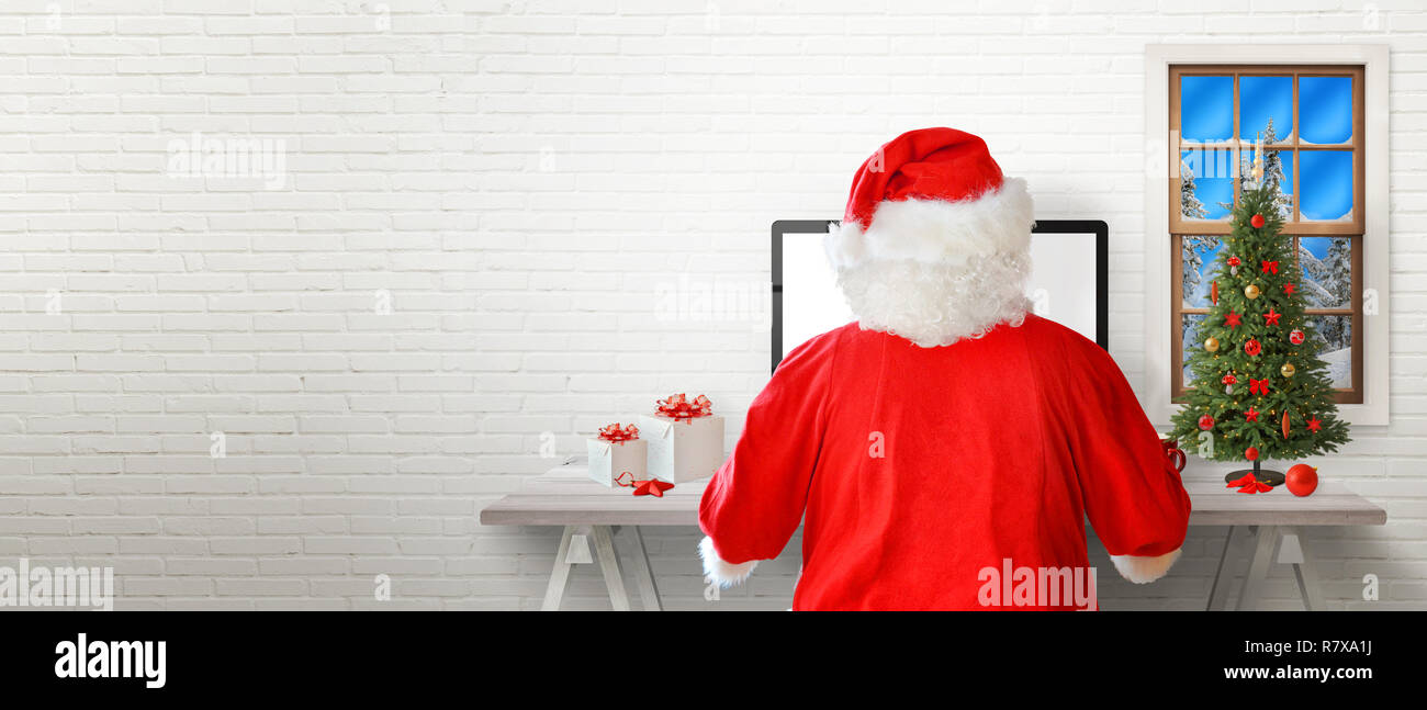 Santa arbeiten auf einem Computer in seinem Zimmer. Weiße Wand im Hintergrund mit einem freien Text. Stockfoto