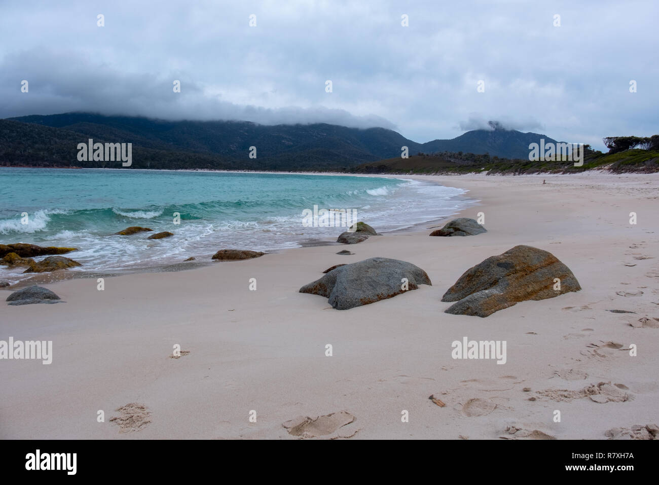 Strand am Wineglass Bay, Freycinet Nationalpark, Tasmanien mit Steinen in den Vordergrund und blaues Meer an einem bewölkten Tag Stockfoto