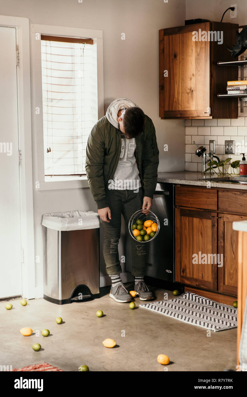 Verärgert und Besiegte junger Erwachsener Person versehentlich verschüttete Flüssigkeiten Korb von Zitronen und Limetten Obst alle über moderne Küche zu Hause und hat eine traurige Gefühl Stockfoto