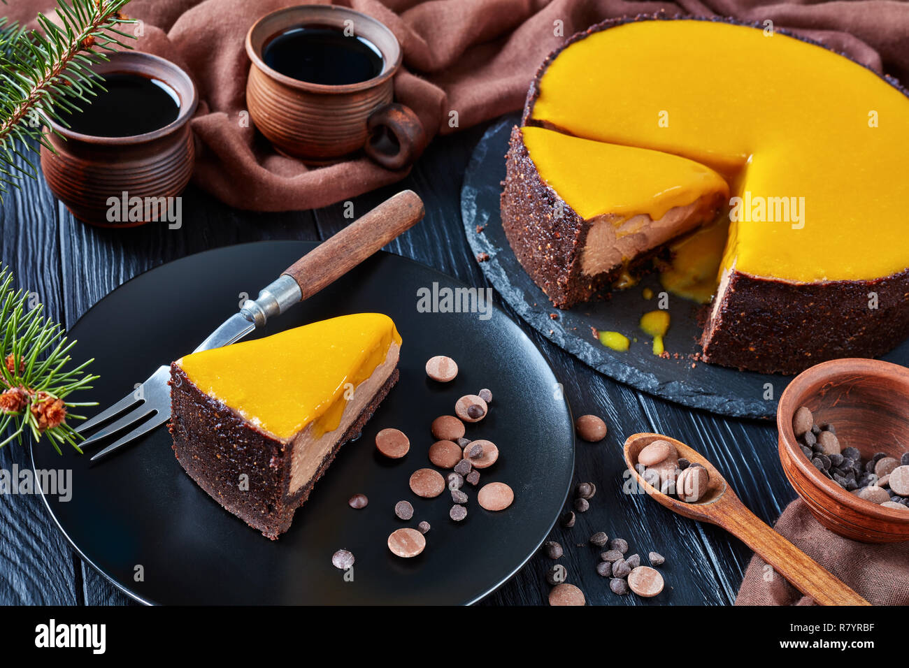 In Scheiben geschnittene Schokolade Mango cheesecake. ein Stück Kuchen auf eine schwarze Platte mit Dessert Gabel und Chocolate Chips serviert. Tanne und Tassen mit Kaffee auf einem Stockfoto