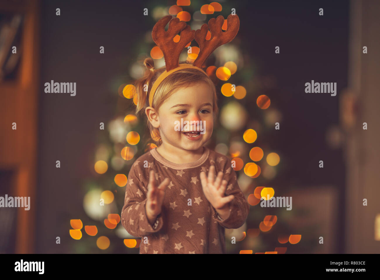 Porträt eines niedlichen kleinen Kind Spaß an Kid's Christmas Party, baby boy Rudolph tragen Hörner, Lachen und Klatschen zu Hause in der Nähe von glühenden Christus Stockfoto