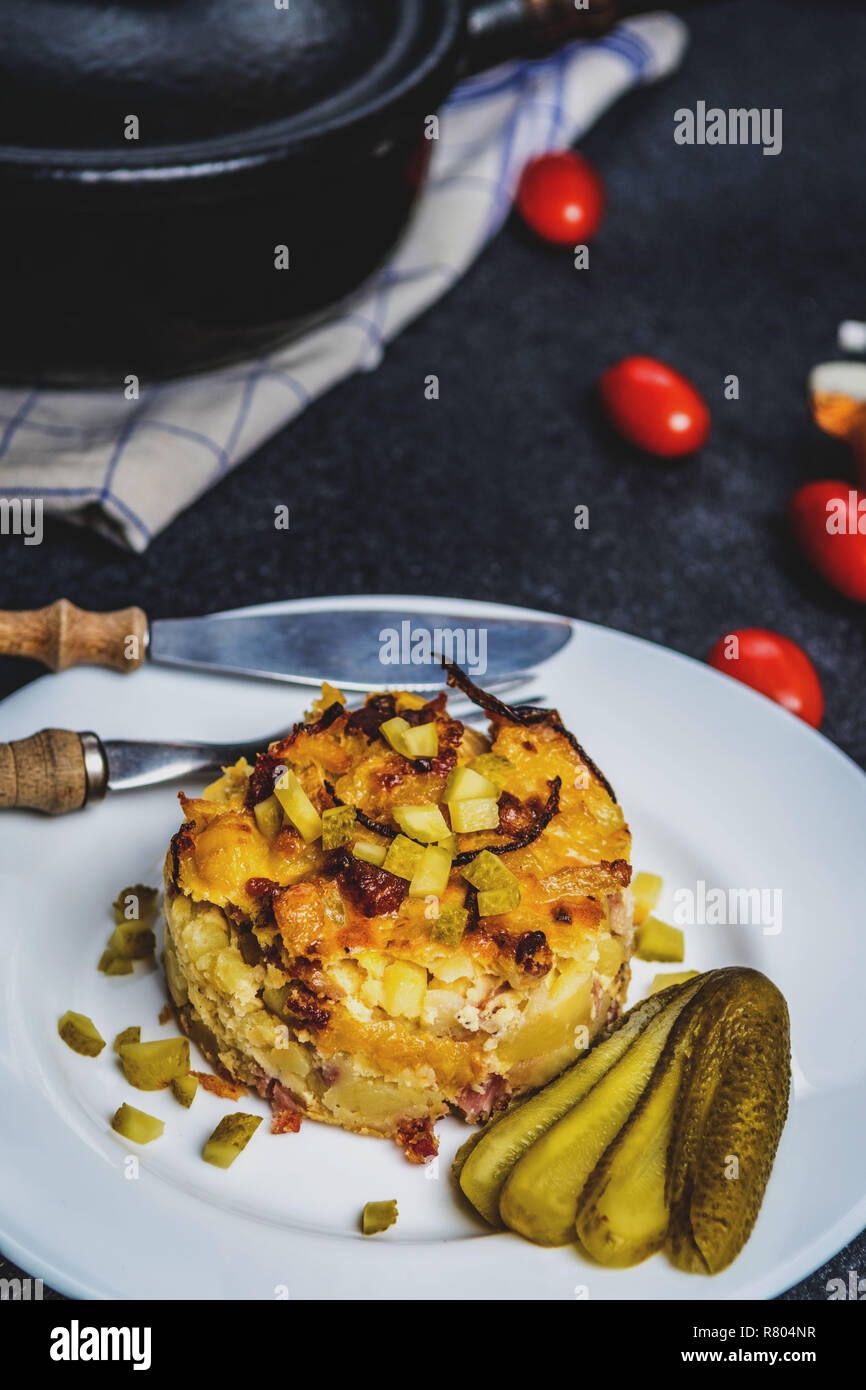 Kartoffelgratin mit Zwiebel und Gurke auf weiße Platte auf schwarzen Steintisch mit Cherry Tomaten. Tschechische traditionelle Küche Stockfoto