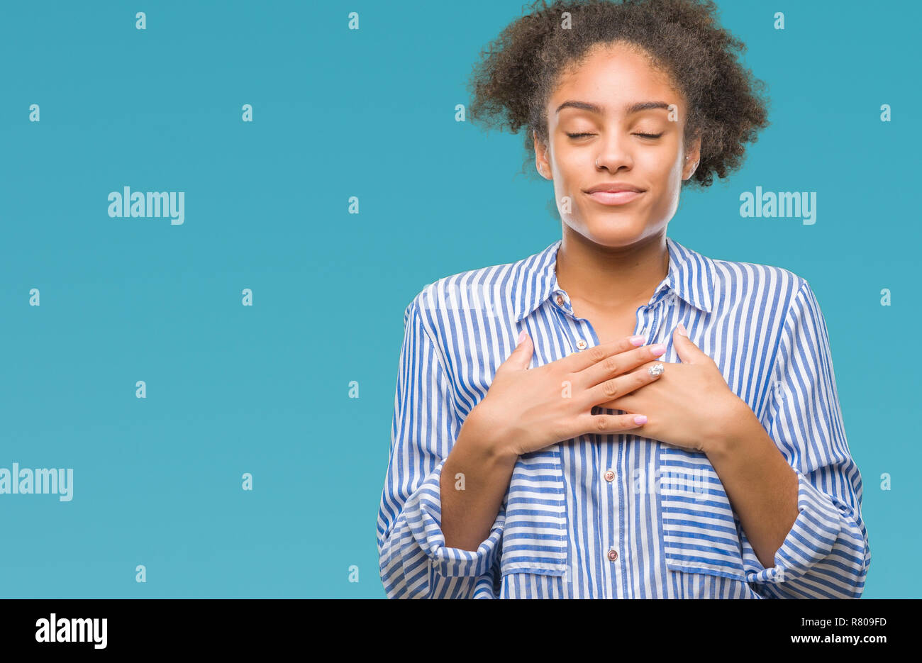 Junge afro-amerikanische Frau über isolierte Hintergrund lächelnd mit der Hand auf der Brust mit geschlossenen Augen und dankbare Geste auf das Gesicht. Gesundheit Konzept. Stockfoto