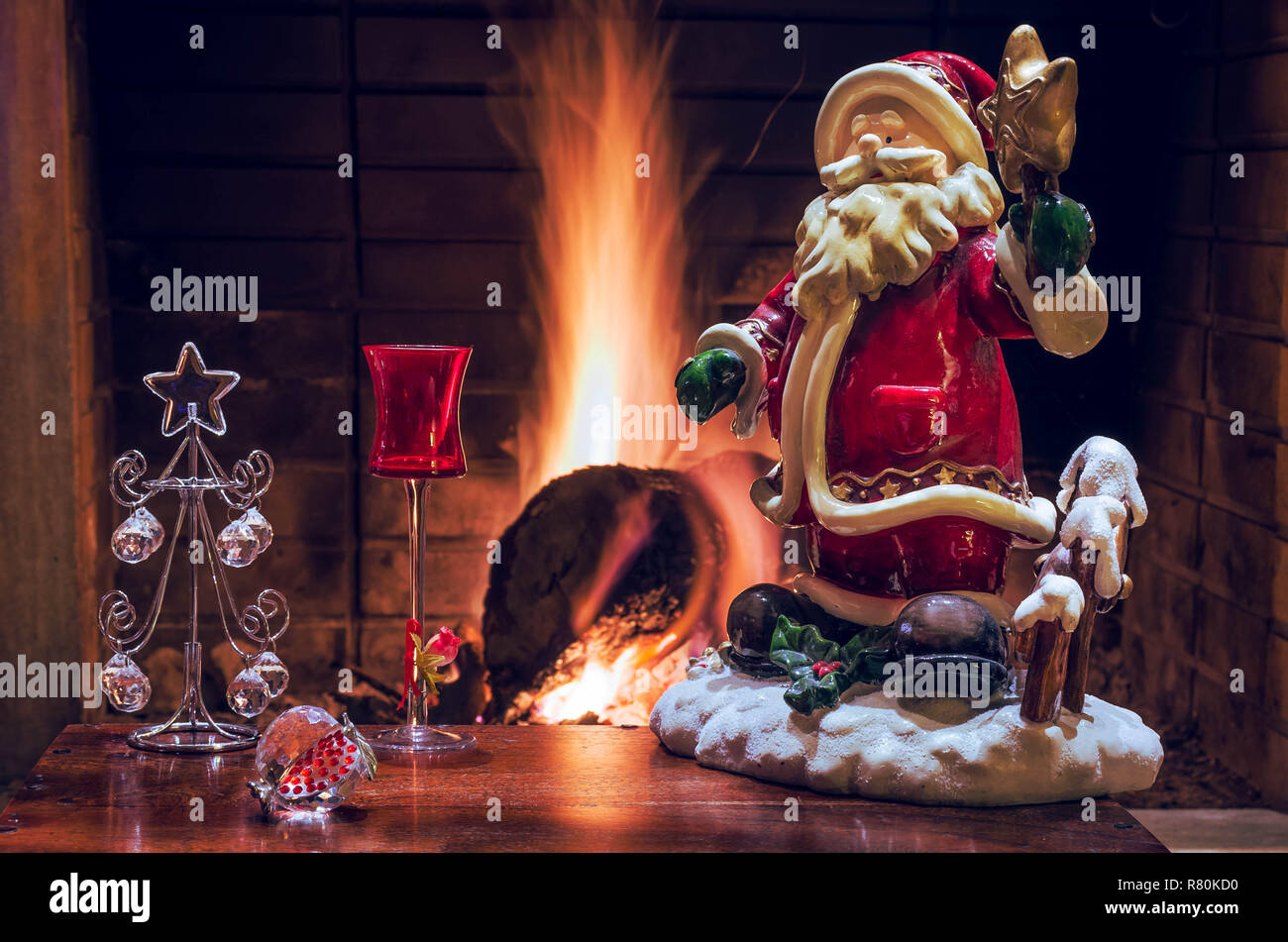 Weihnachtsdekoration mit Santa Claus, Crystal Christmas Tree, rot Likör Glas und Granatapfel. Die Flamme der Kamin im Hintergrund. Stockfoto