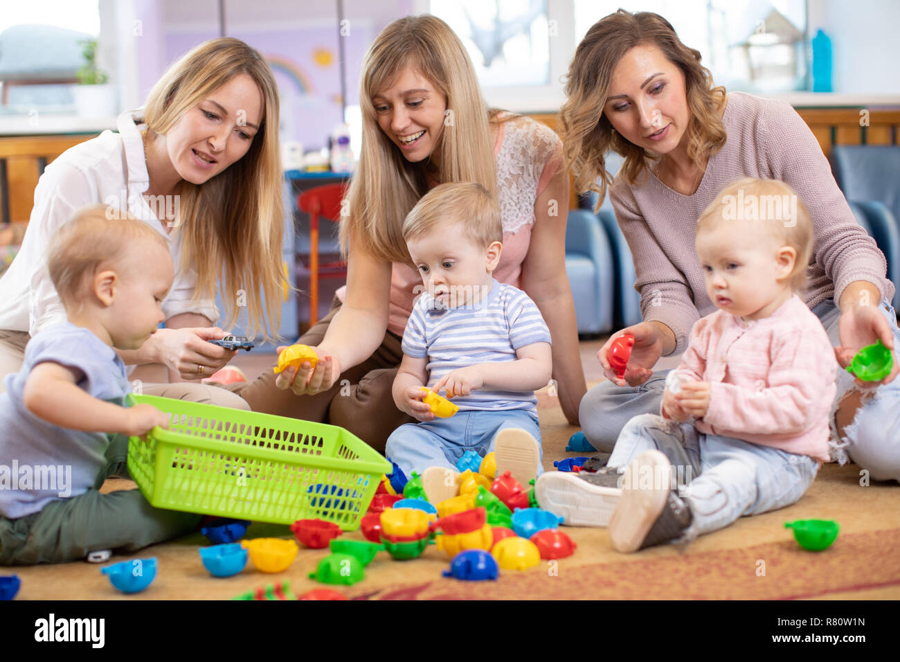 Gruppe von Kindern 1-2 Jahre alt, spielen im Kindergarten oder in der Kindertagesstätte unter der Aufsicht von Mammen Stockfoto