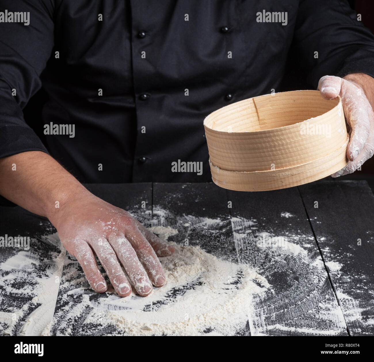 Küchenchef bereitet den Teig aus weissem Mehl, in Ihrer Hand runden hölzernen Sieb Stockfoto