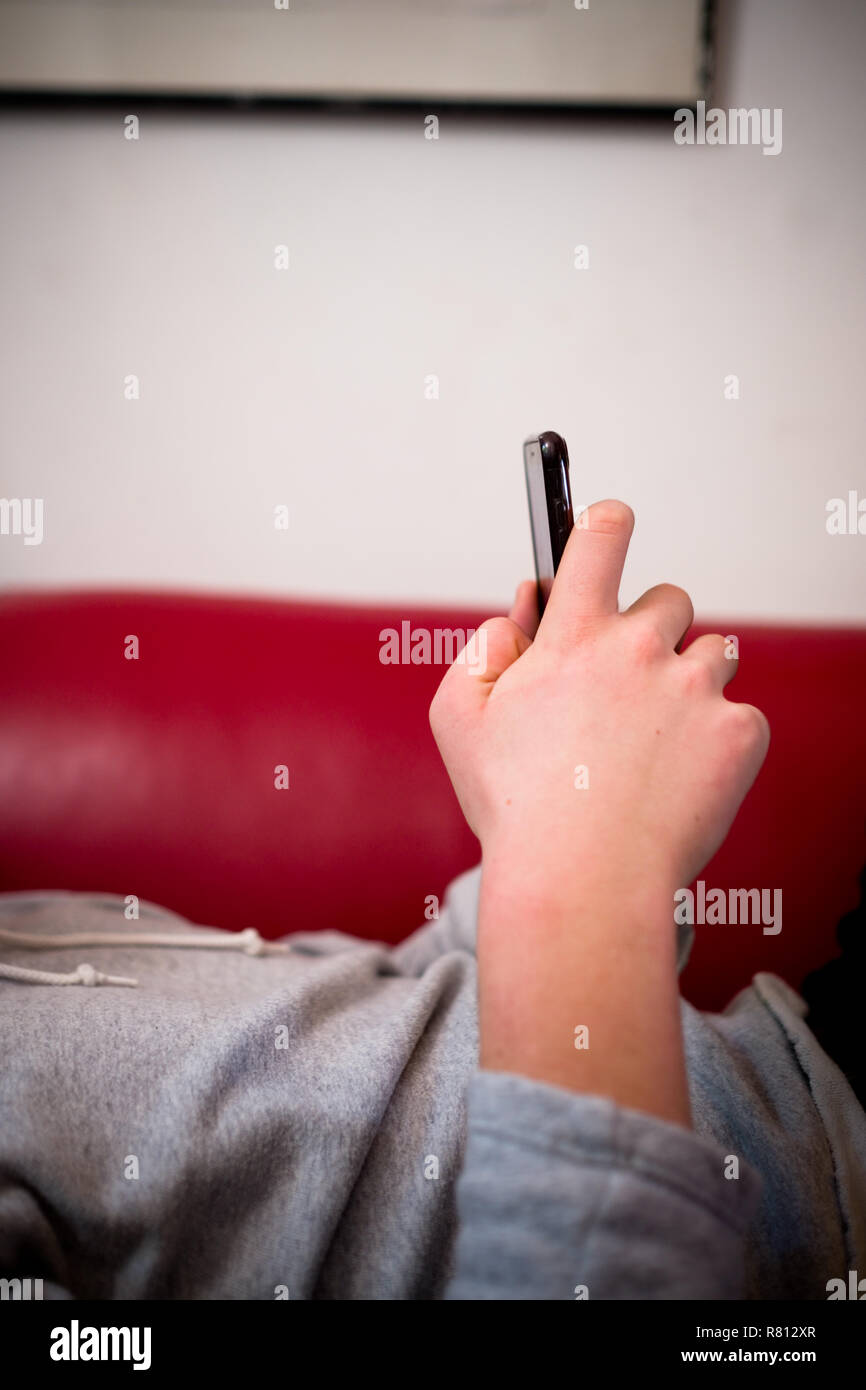 Nahaufnahme Seitenansicht der Hände eines jungen Mann mit einem Smartphone, während er auf einem roten Sofa in einer häuslichen Umgebung Stockfoto
