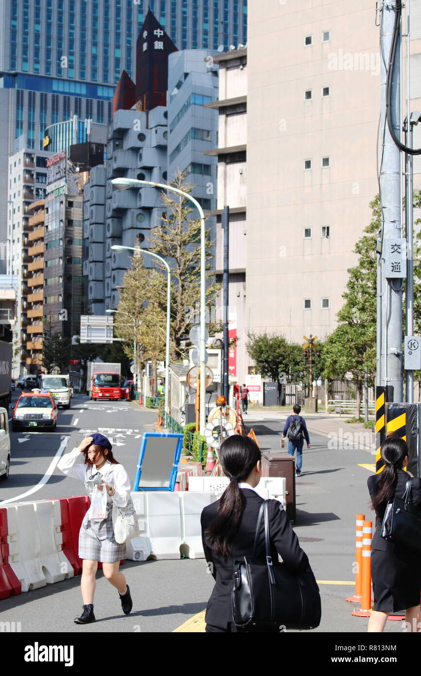 Eine Straße am Rande des Tokyo Shimbashi Bereich an einem windigen Tag mit dem Wahrzeichen Nakagin Capsule Tower und moderne Gebäude im Hintergrund. Stockfoto