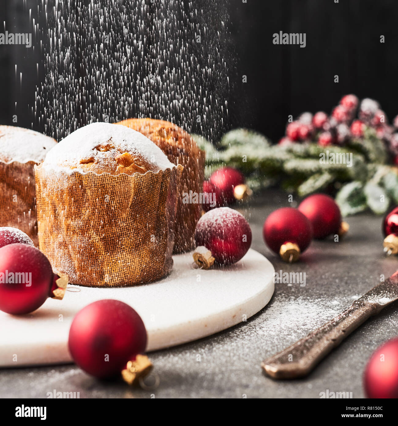 Besprengung Puderzucker über traditionelle Weihnachten mini Panettone mit Rosinen und getrocknete Früchte auf weißem Marmor Servierteller umgeben von roten baub Stockfoto