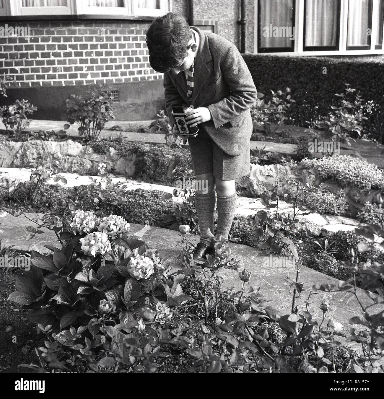 1950, historische, Film, Fotografie, ein schuljunge außerhalb einen Blumengarten, die Bilder von Blumen mit einer Kodak "Brownie" Reflex Film Kamera, England, UK. Ein fester Fokus, twin-lens Kamera, es war eine einfache, aber beliebter Kamera der Epoche, insbesondere mit denen ab, die in der Fotografie. Stockfoto