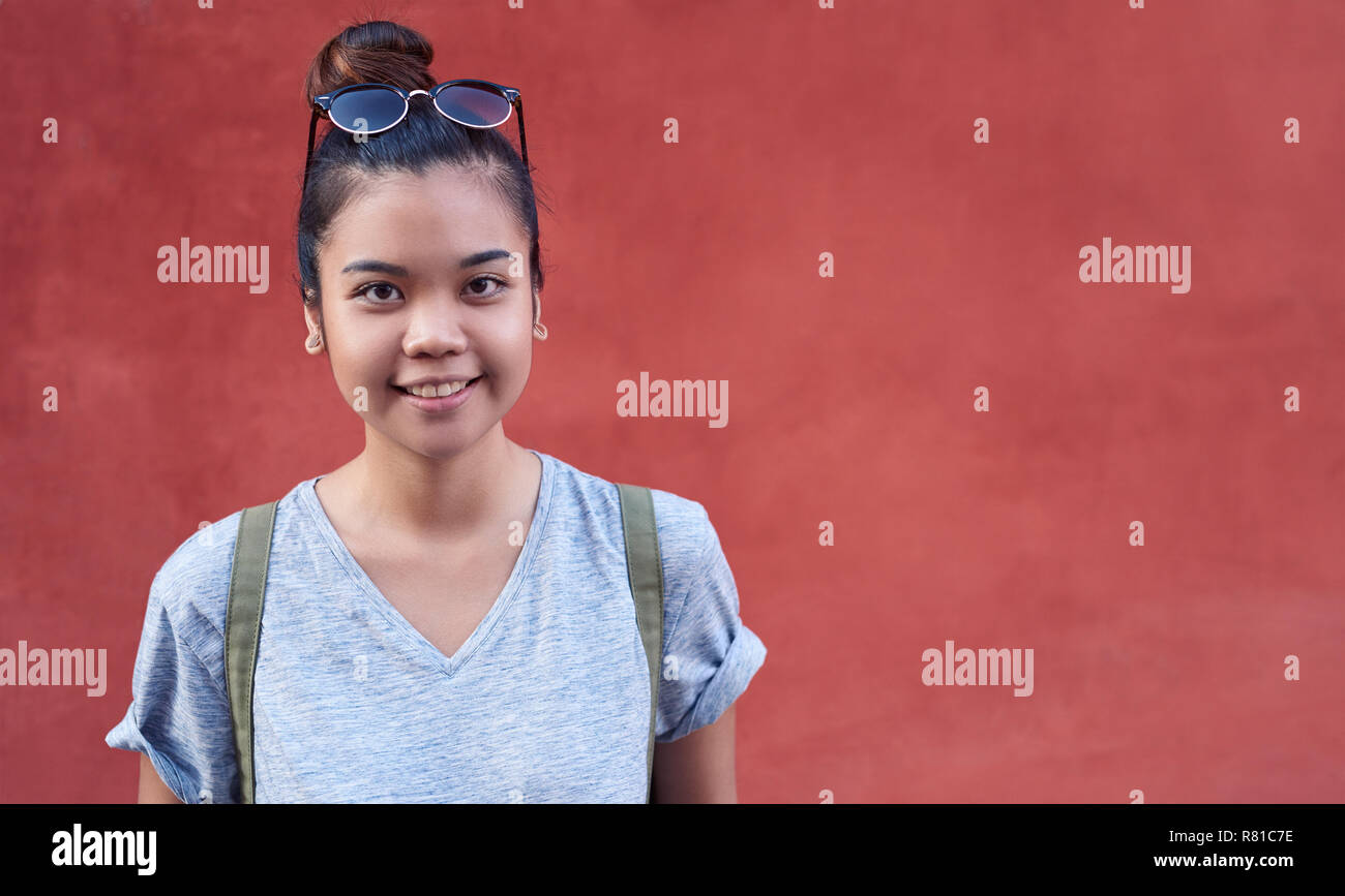Lächelnde junge asiatische Frau durch eine Wand draußen stehen Stockfoto