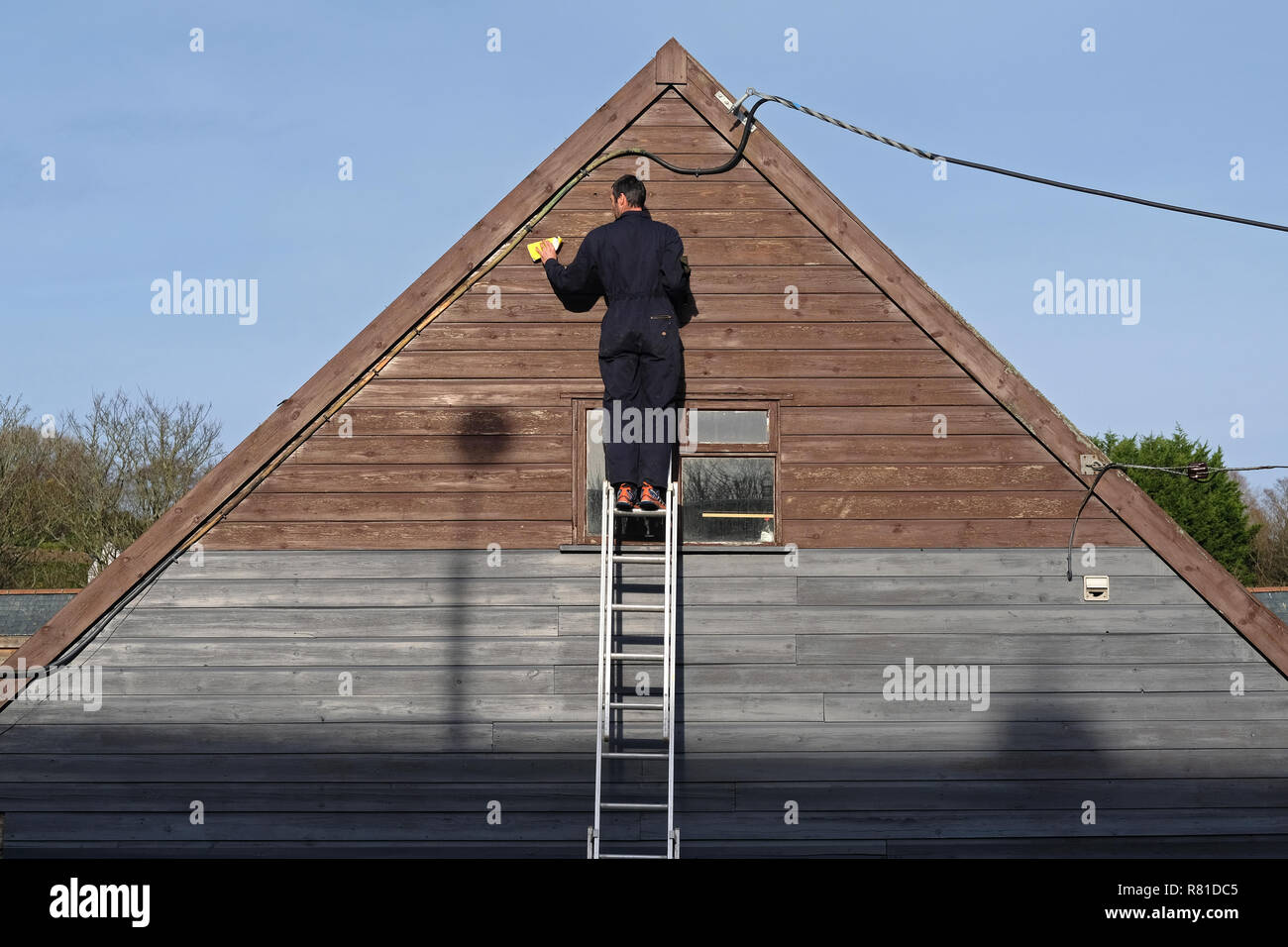 Ein Tischler, Dekorateur, nach unten Schleifen der äußeren Holzarbeit eines Gebäudes. Stockfoto