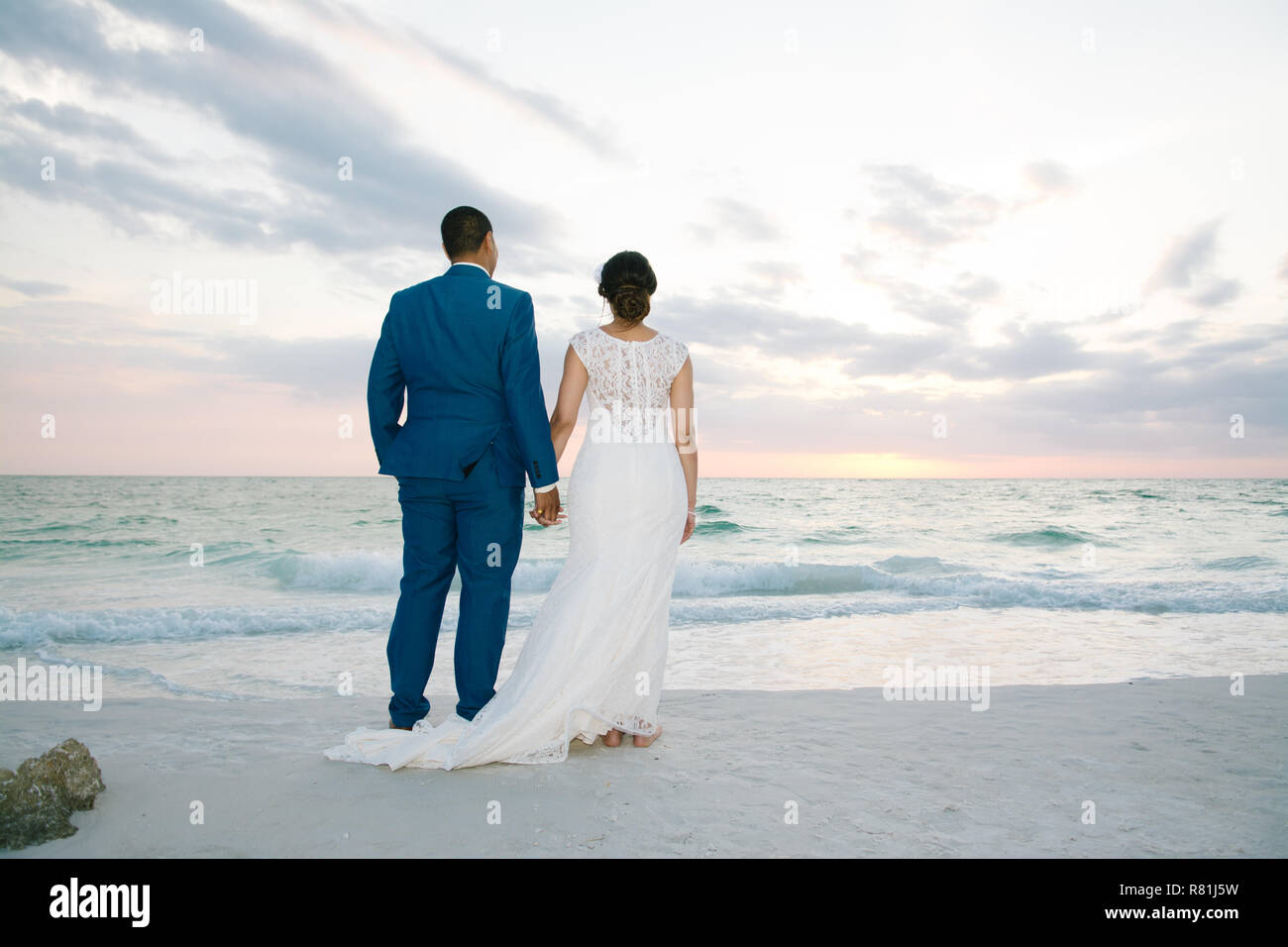 Neu jungen verheirateten männlichen Mann und Frau Frau, Hände auf den Strand mit Blick auf das Meer Horizont bei Sentset nach Hochzeit Stockfoto
