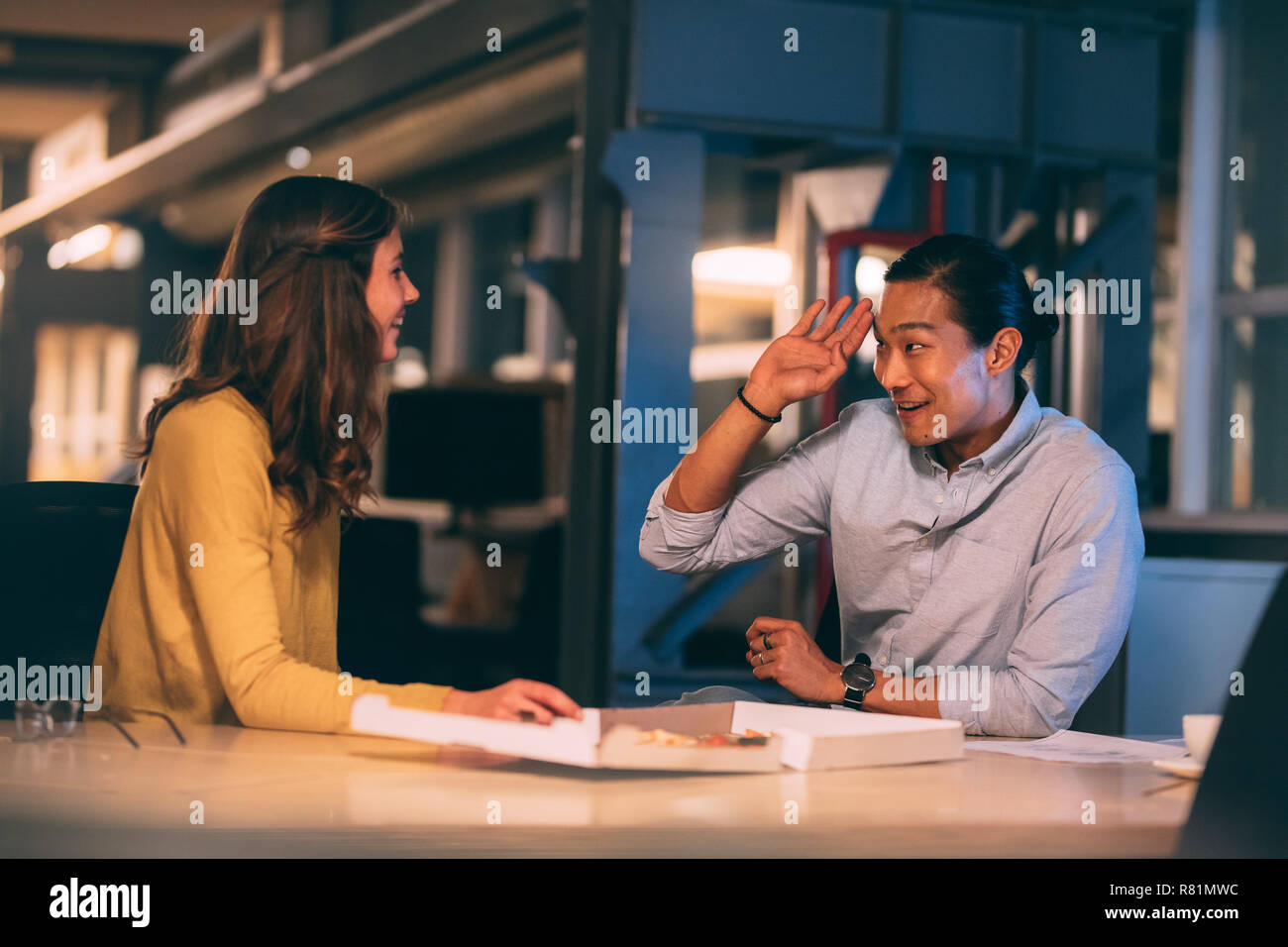 Lächelnd asiatische Geschäftsmann sitzt mit einer Kollegin im Büro essen Pizza. Freundliche Geschäftspartner sitzen spät im Büro Essen. Stockfoto