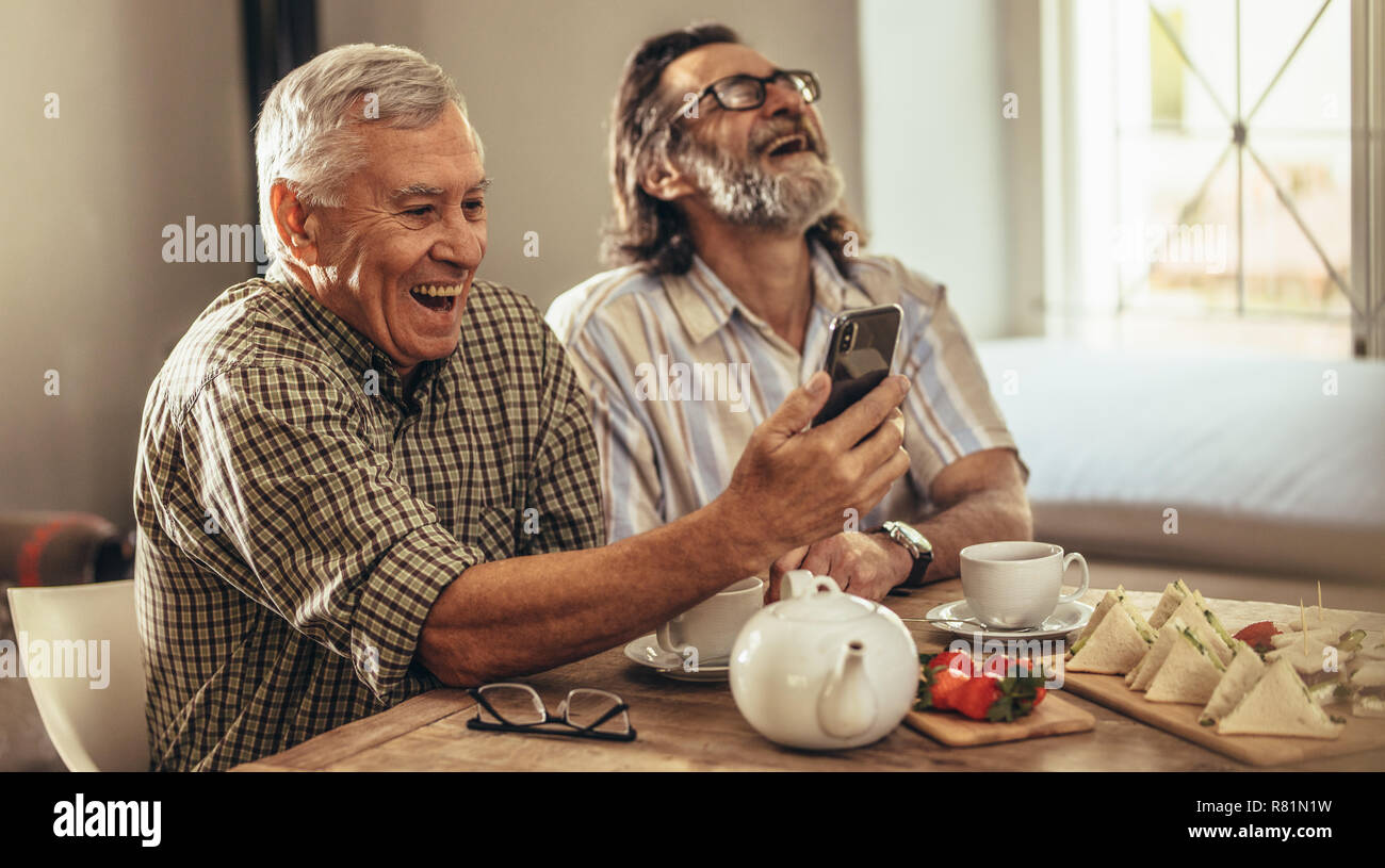 Zwei glücklich pensionierte Männer Suchen in alten Fotografien zusammen und Lachen. Reife männliche Freunde zu Hause genießen, während sich Ihre alte Erinnerungen auf Sm suchen Stockfoto